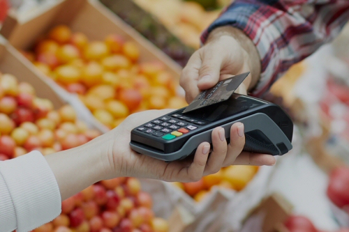 Close-up of a customer tapping a credit card on a handheld Sunfire POS terminal to complete a purchase.